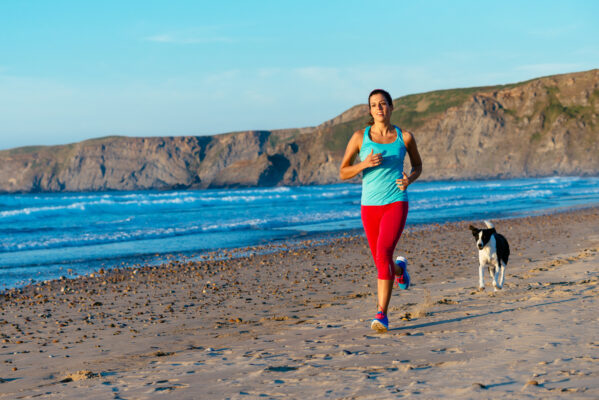 Frau beim Joggen mit Hund am Strand