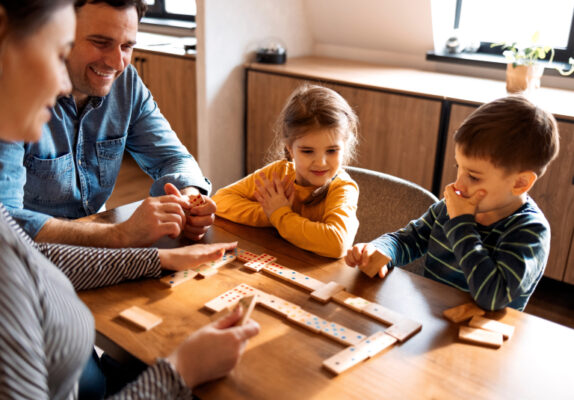 Eine Familie mit 2 Kindern spielt am Tisch ein Spiel.