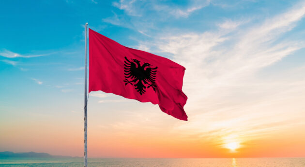 Albanien Flagge weht im Wind vor Sonne und Meer